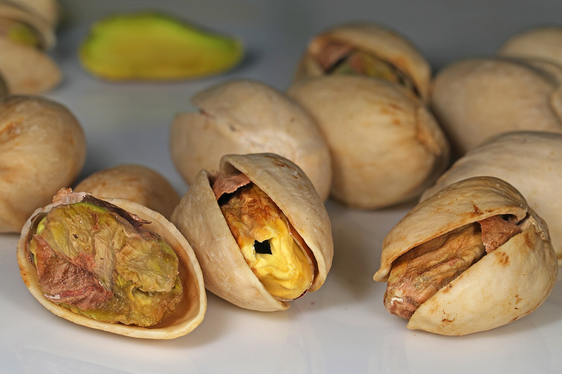 Whole pistachios in their split cream-coloured shells, one open to show the green kernel inside