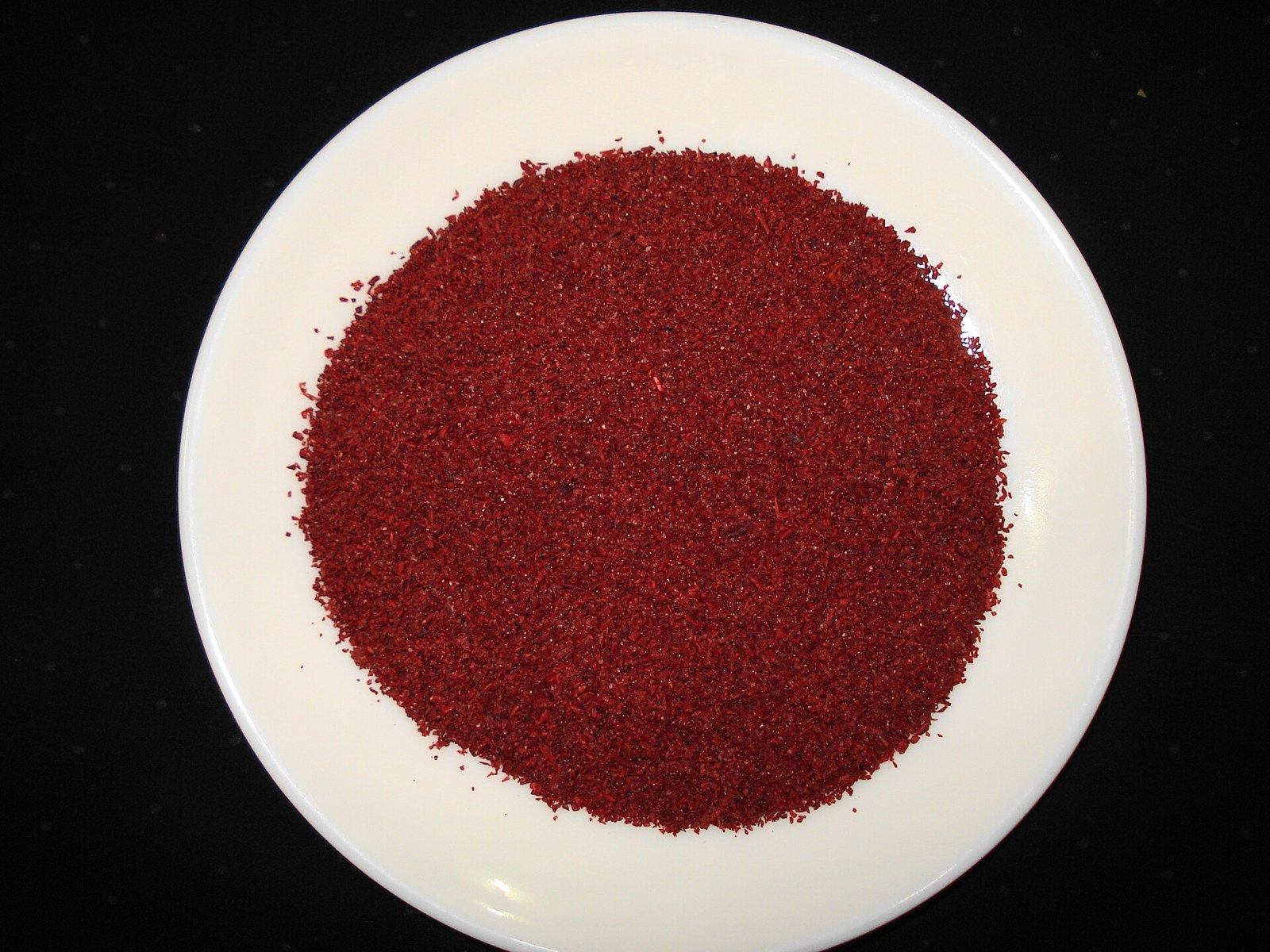 A white plate filled with coarsely ground deep crimson sumac powder