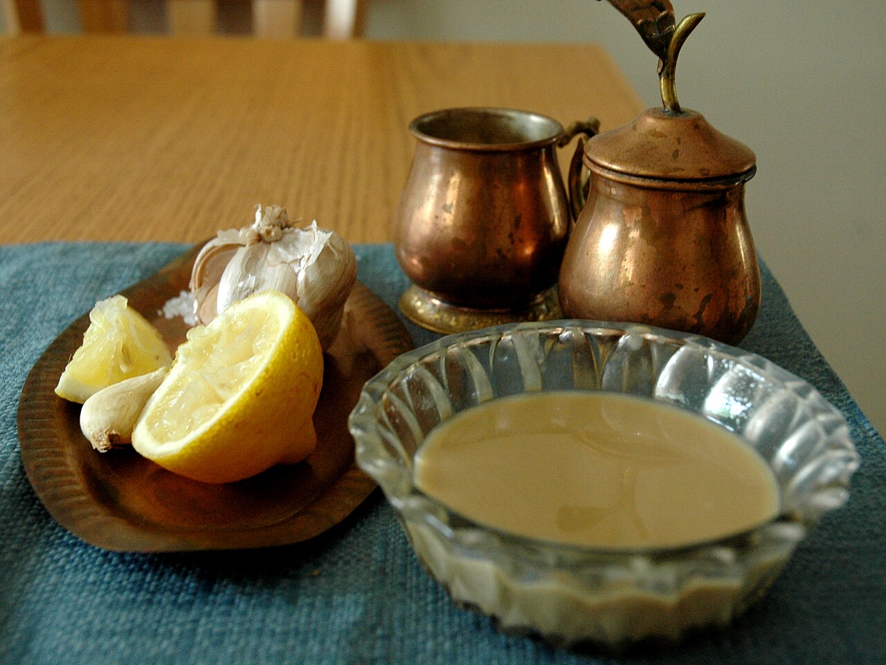 A glass bowl of pale tan tahini beside lemon and garlic