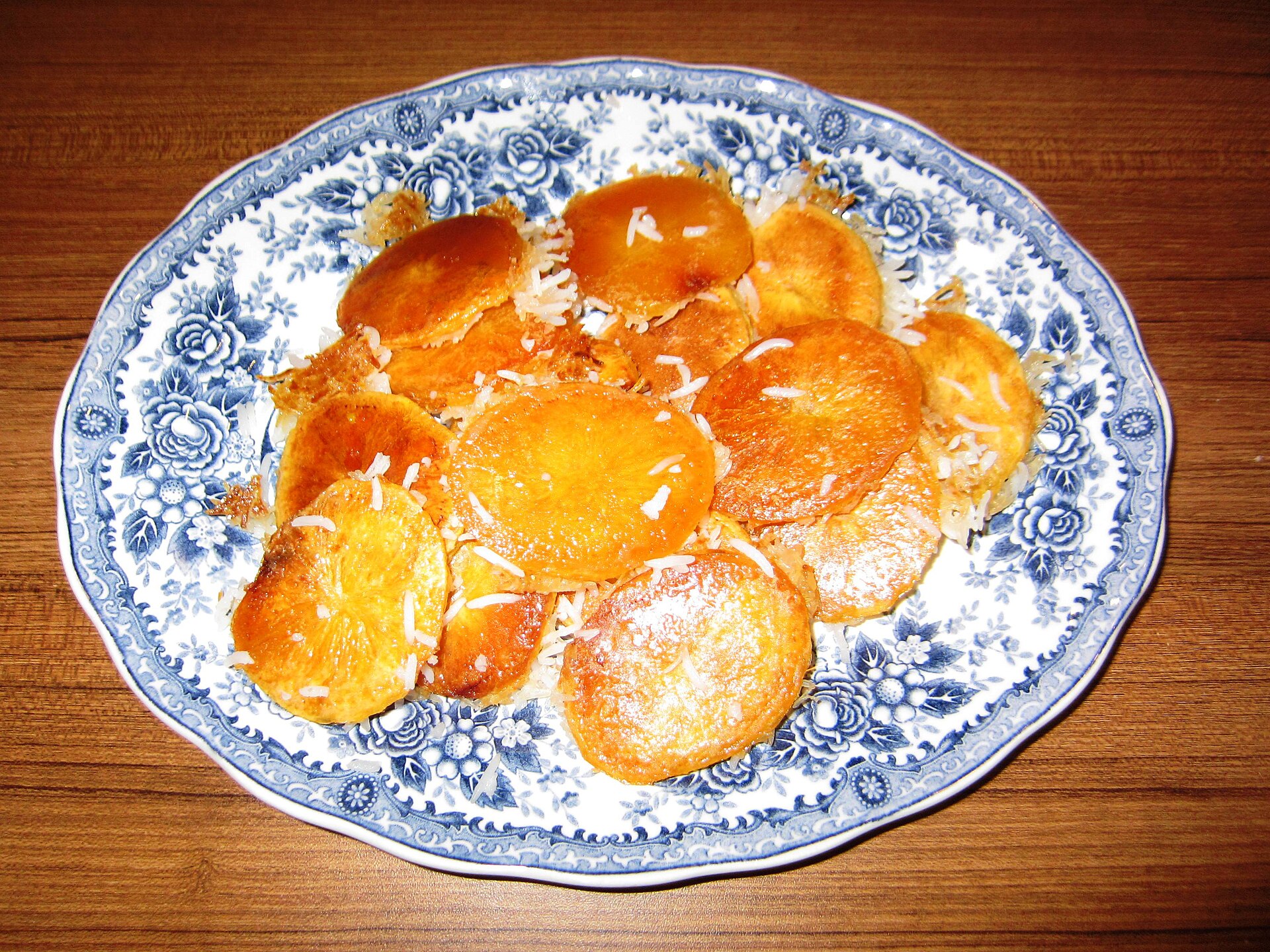 Browned rounds of potato tahdig served on a blue-and-white platter.