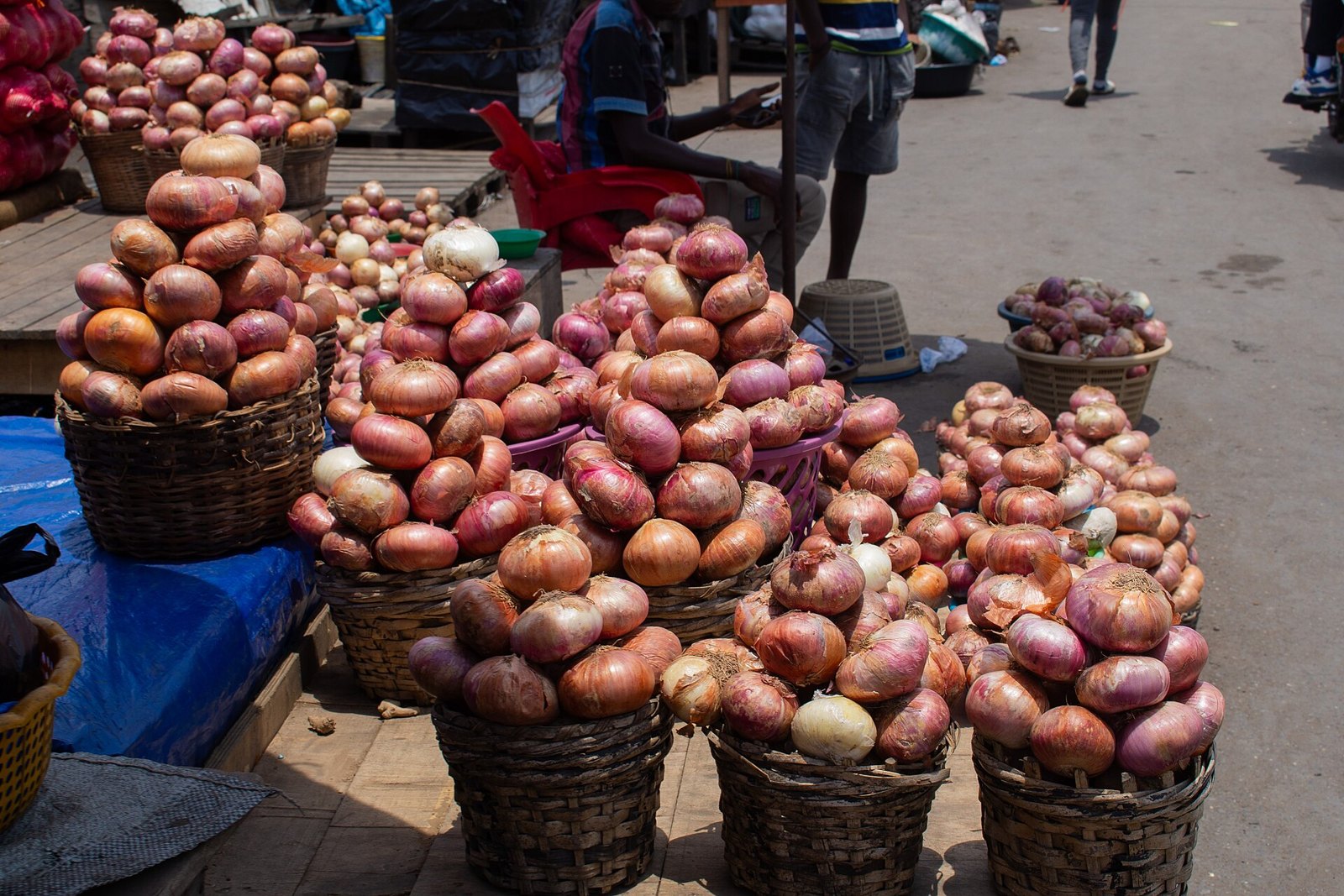 Woven baskets heaped with onions at an open-air market, papery copper and pink-red skins piled high