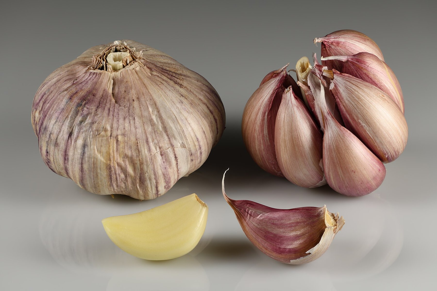 A whole papery garlic bulb beside a split bulb showing its packed purple-skinned cloves, with two loose cloves in front