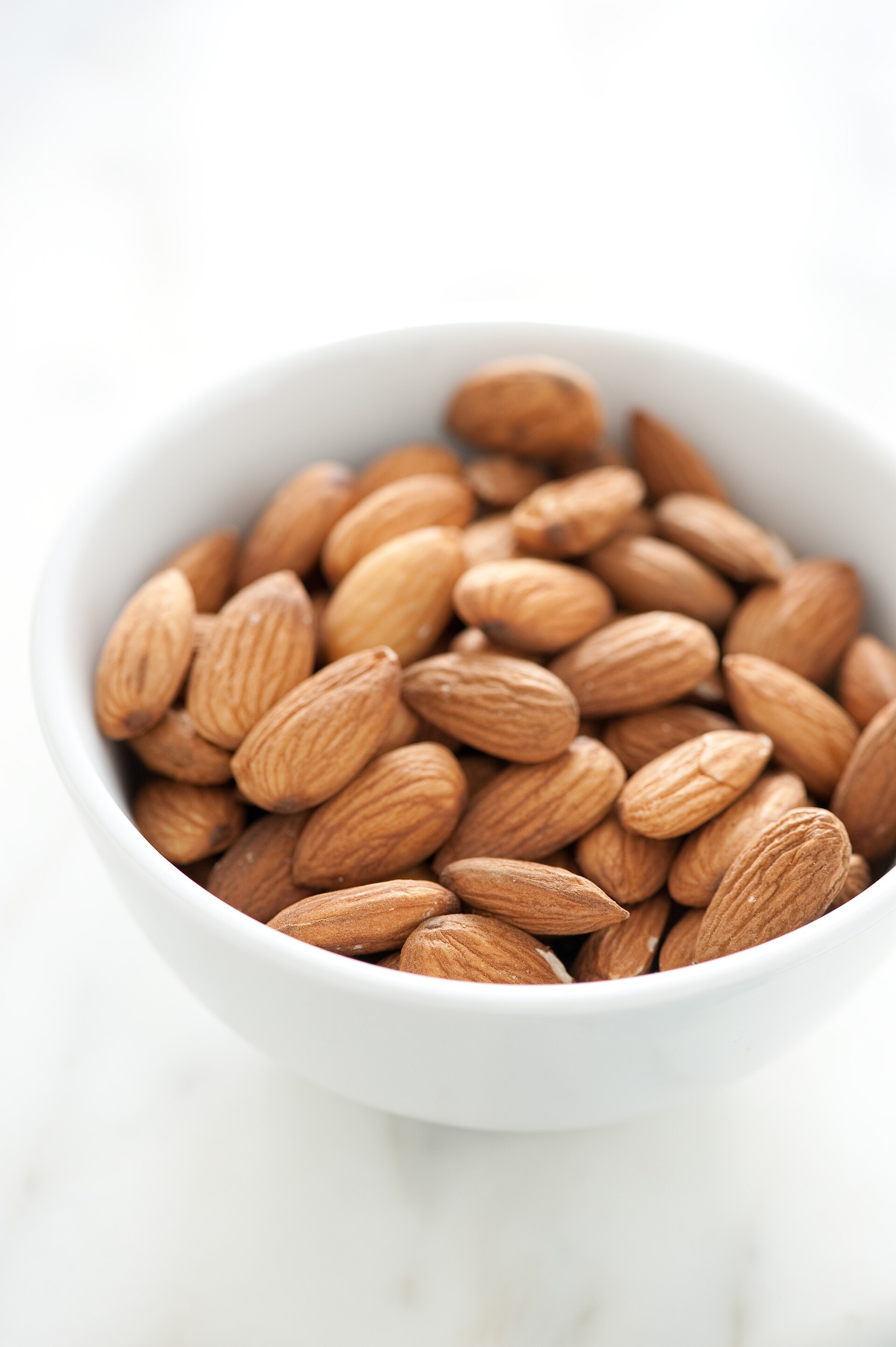 A white bowl filled with whole shelled almonds showing their pale brown skins
