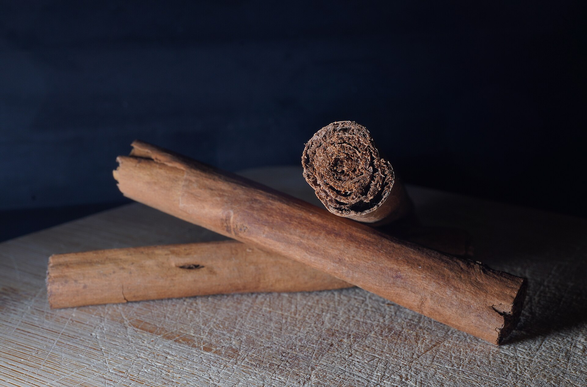 Two whole cinnamon quills resting on a wooden board, one turned end-on to show the bark rolled in tight layers