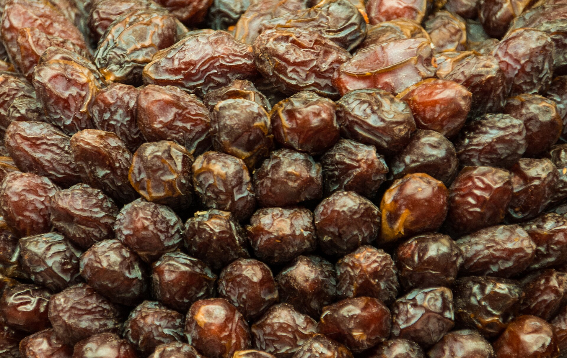 A dense pile of whole dried dates, wrinkled and deep amber-brown, heaped together at a market stall