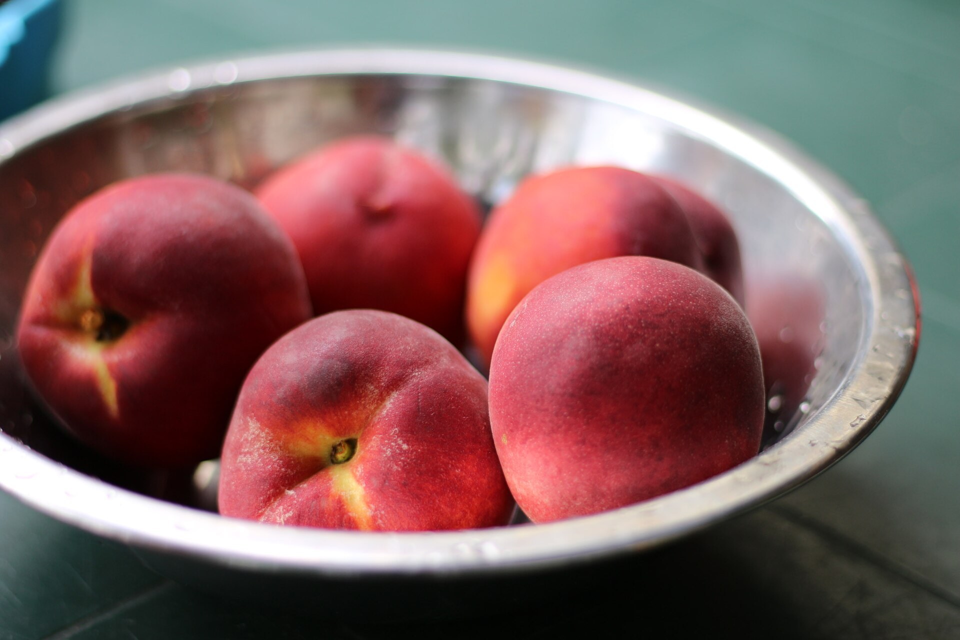 A metal bowl holding four whole ripe peaches with red and gold blushed skin