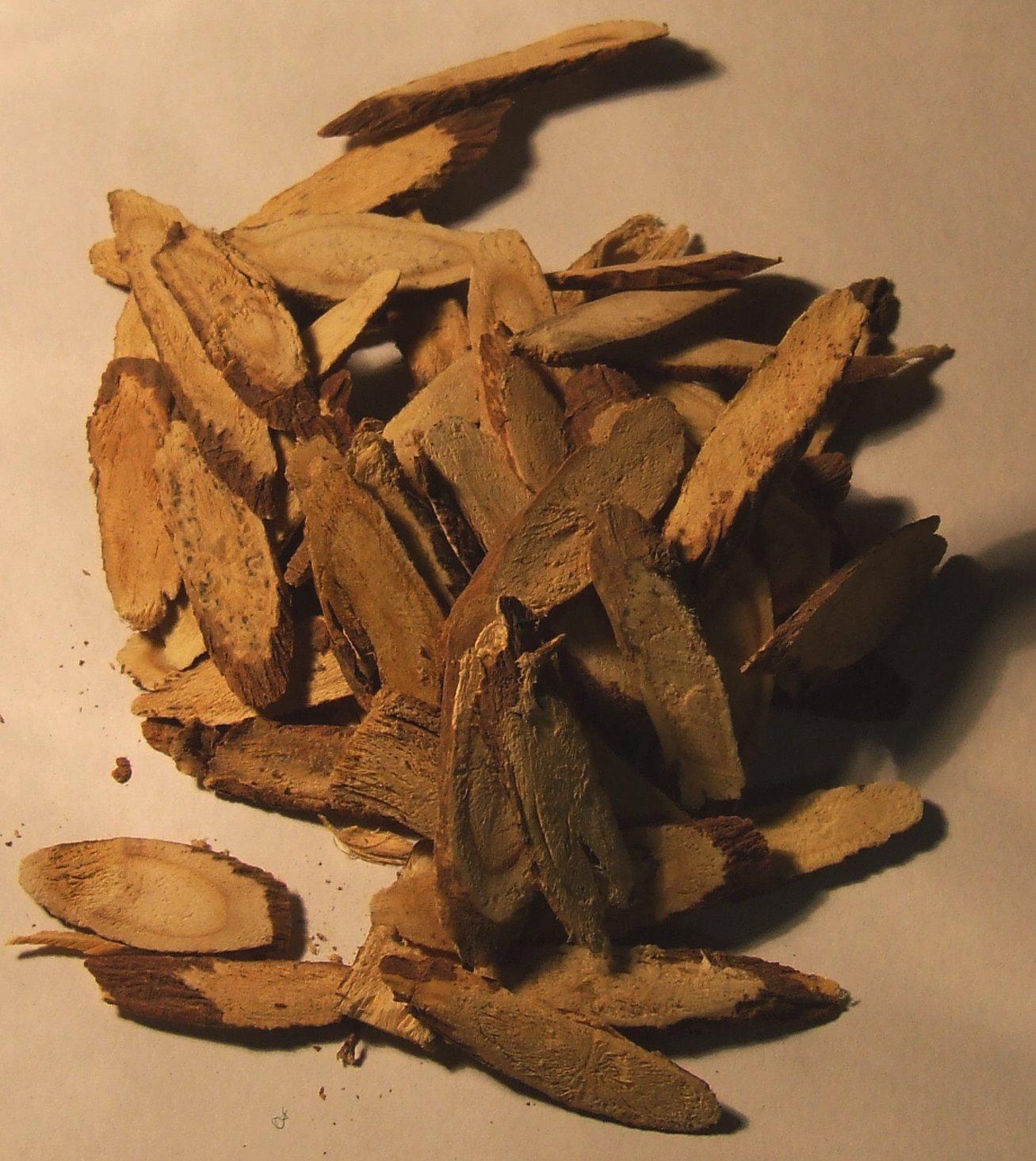 A pile of split licorice root pieces, fibrous yellow inside and rough tan bark outside, resting on a plain background