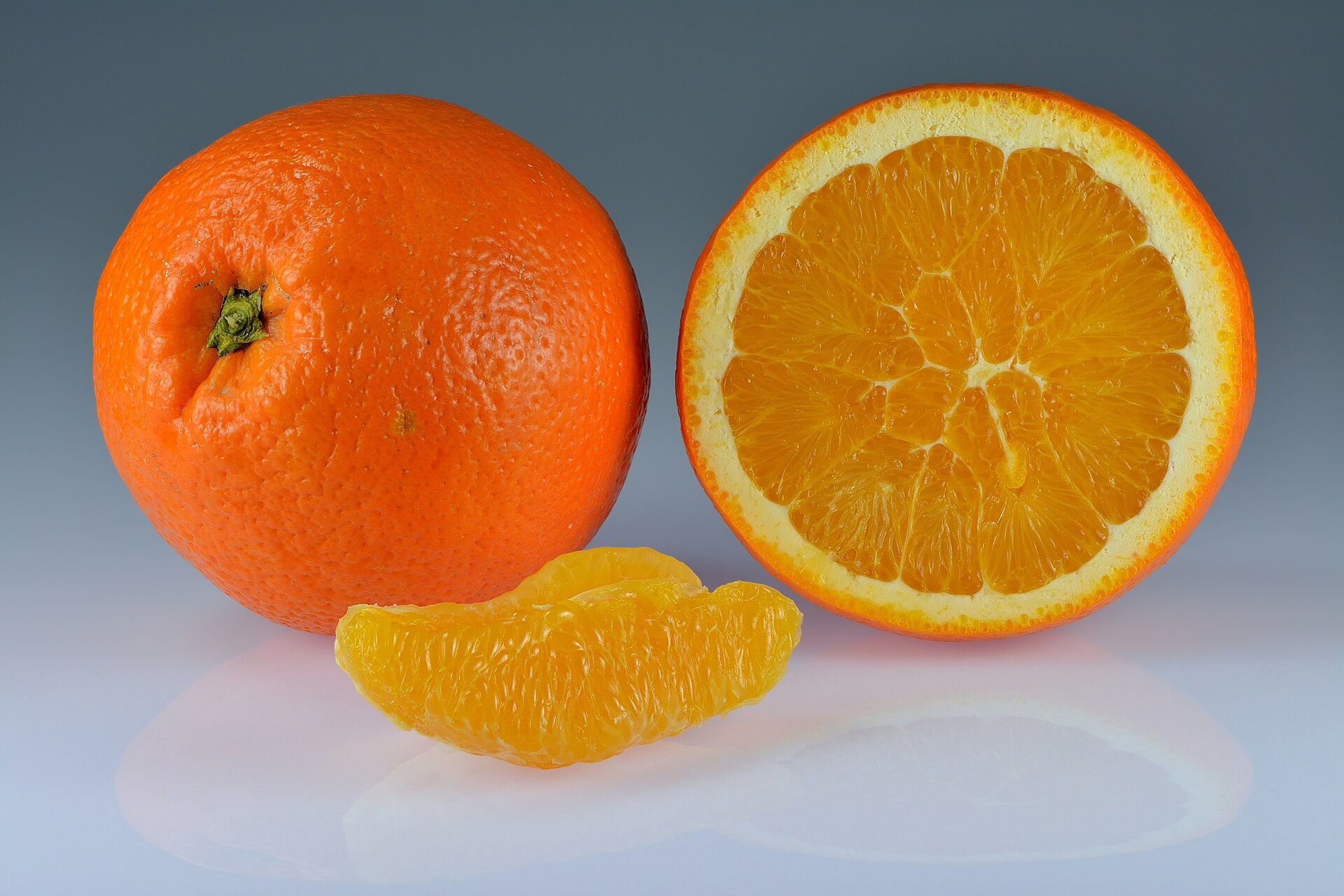 A whole orange beside a halved orange showing its segments, with one loose segment in front