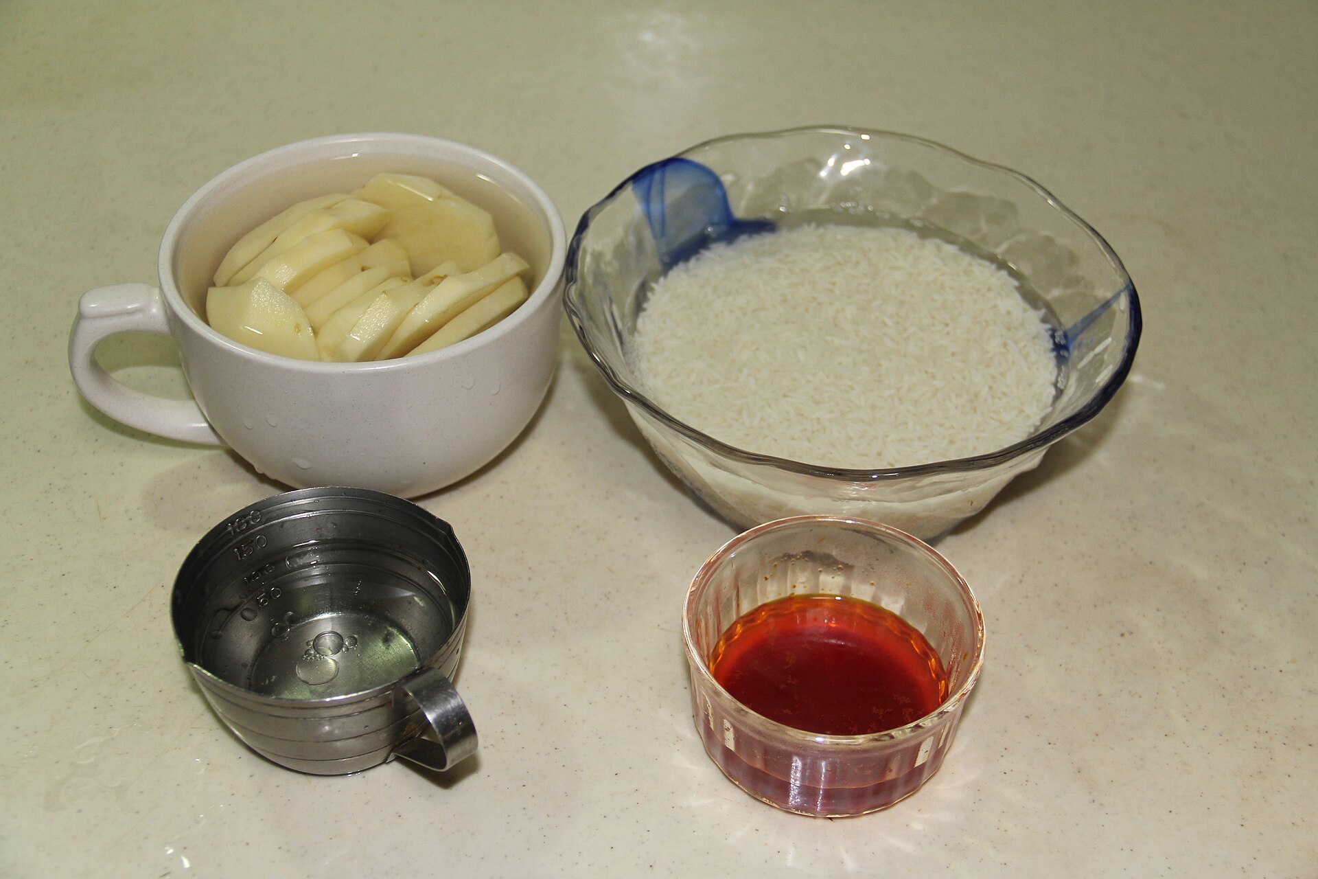 Long-grain rice soaking in a glass bowl beside sliced potato and saffron liquid.