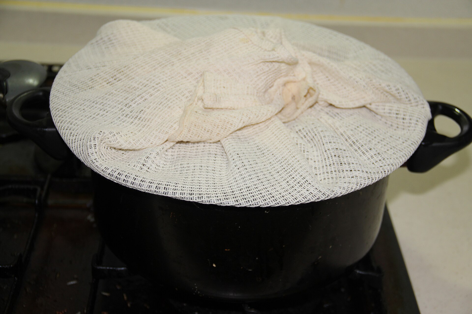 A pot on the stove with its lid covered by a cloth tucked over the top.