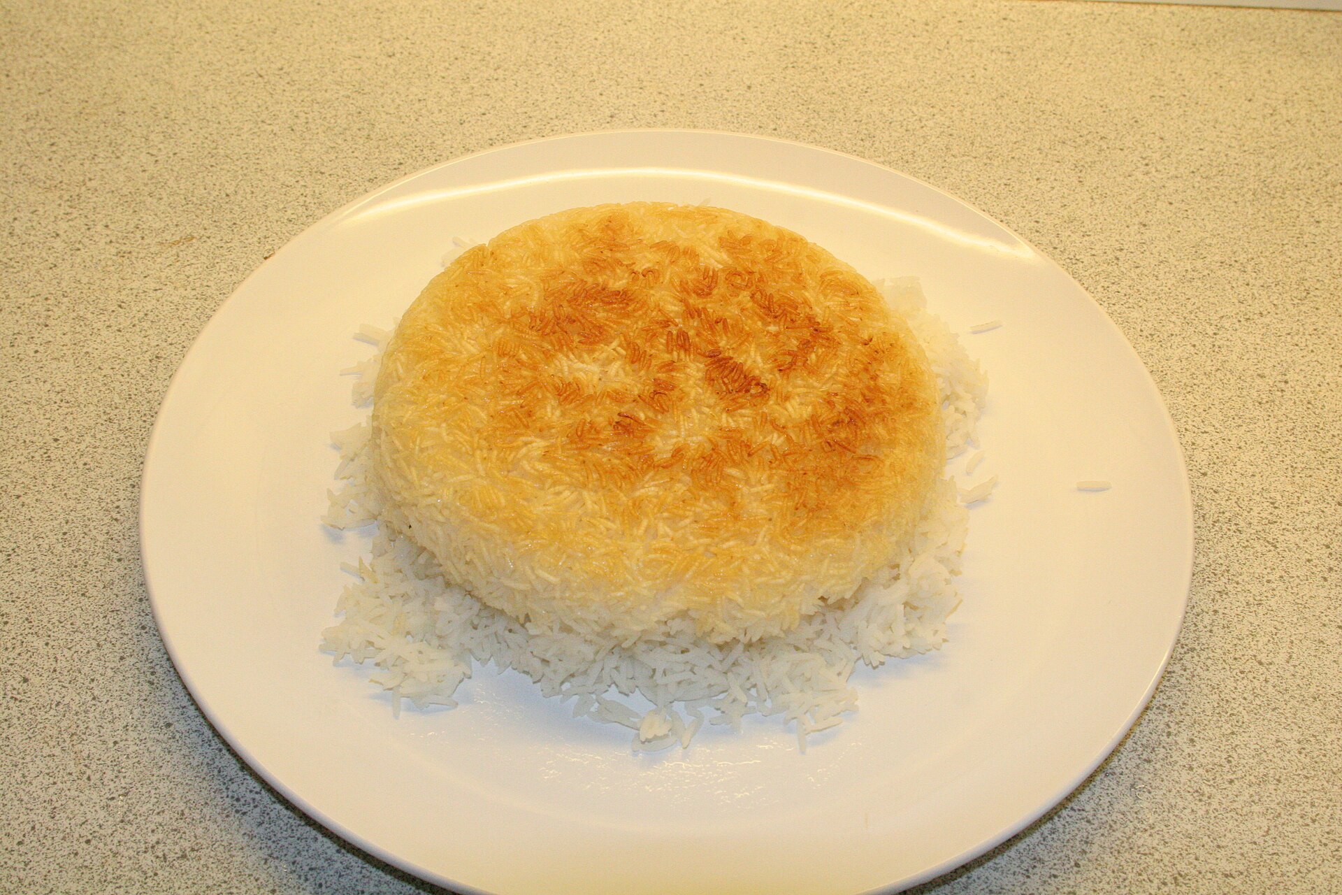 A disc of golden rice crust turned out on a plate over white rice.
