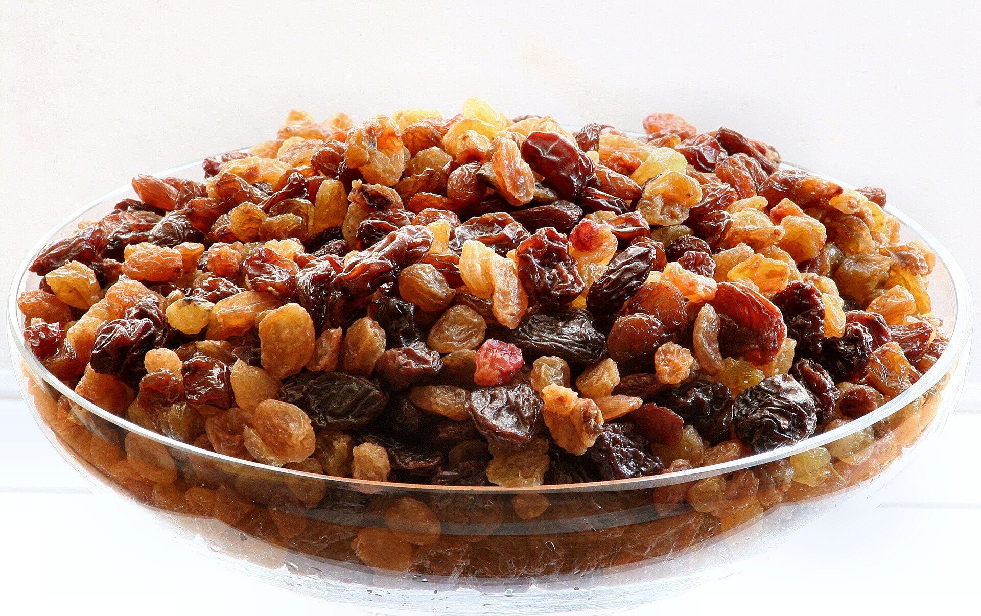 A shallow glass dish heaped with golden and dark brown raisins side by side