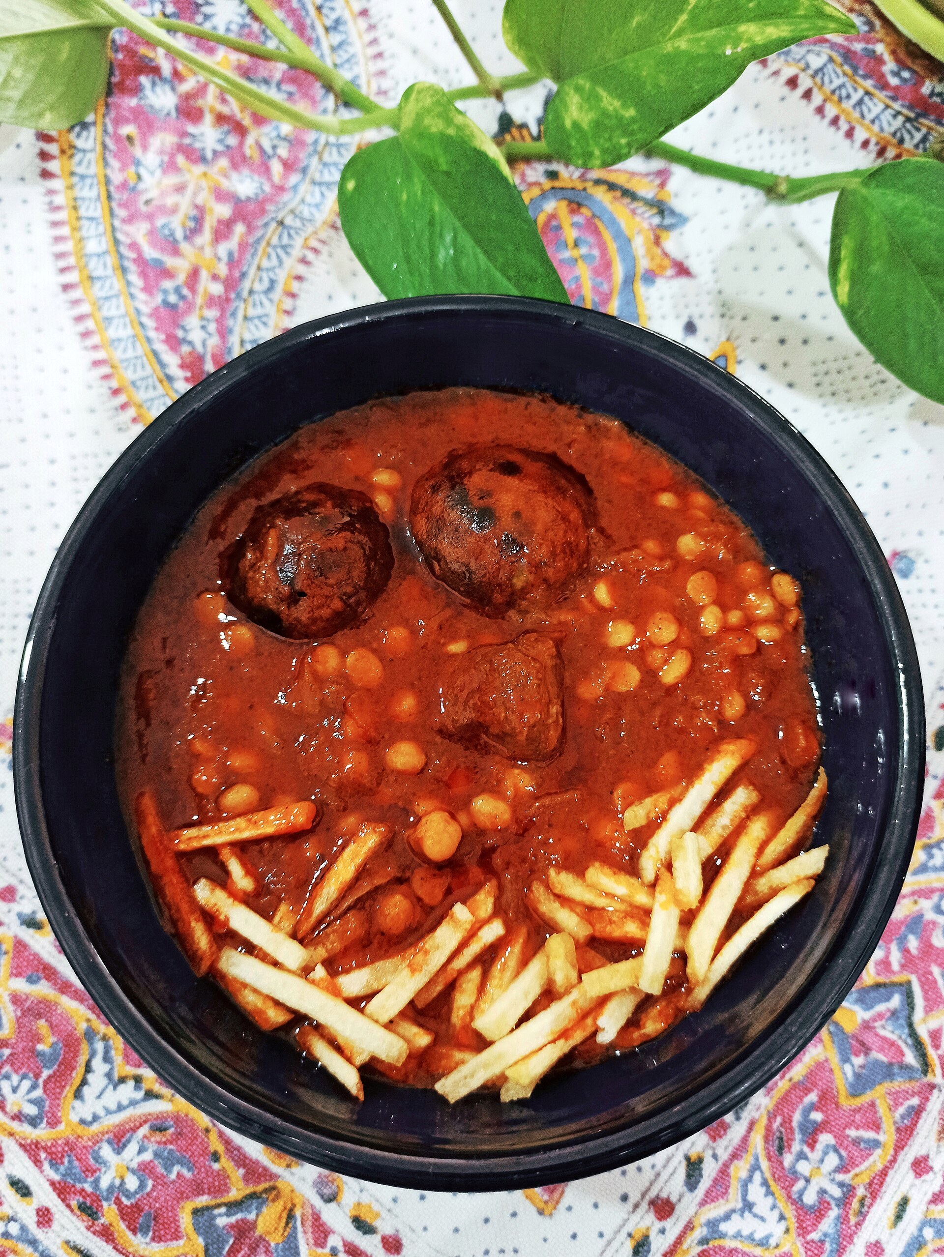 A bowl of gheymeh: yellow split peas and meat in a red tomato sauce with dried limes, topped with crisp fried potato straws.