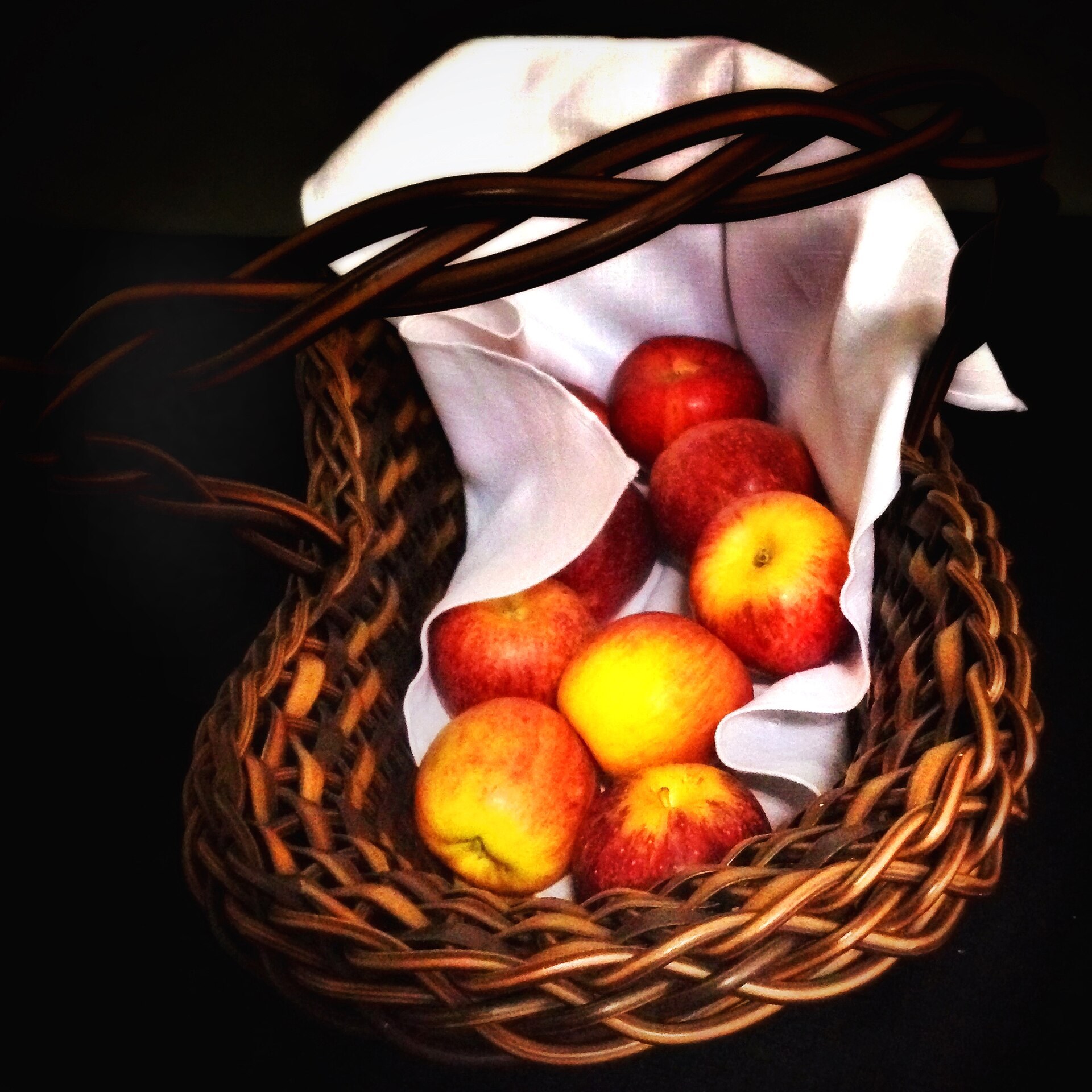 A woven basket lined with cloth holding whole red and yellow apples