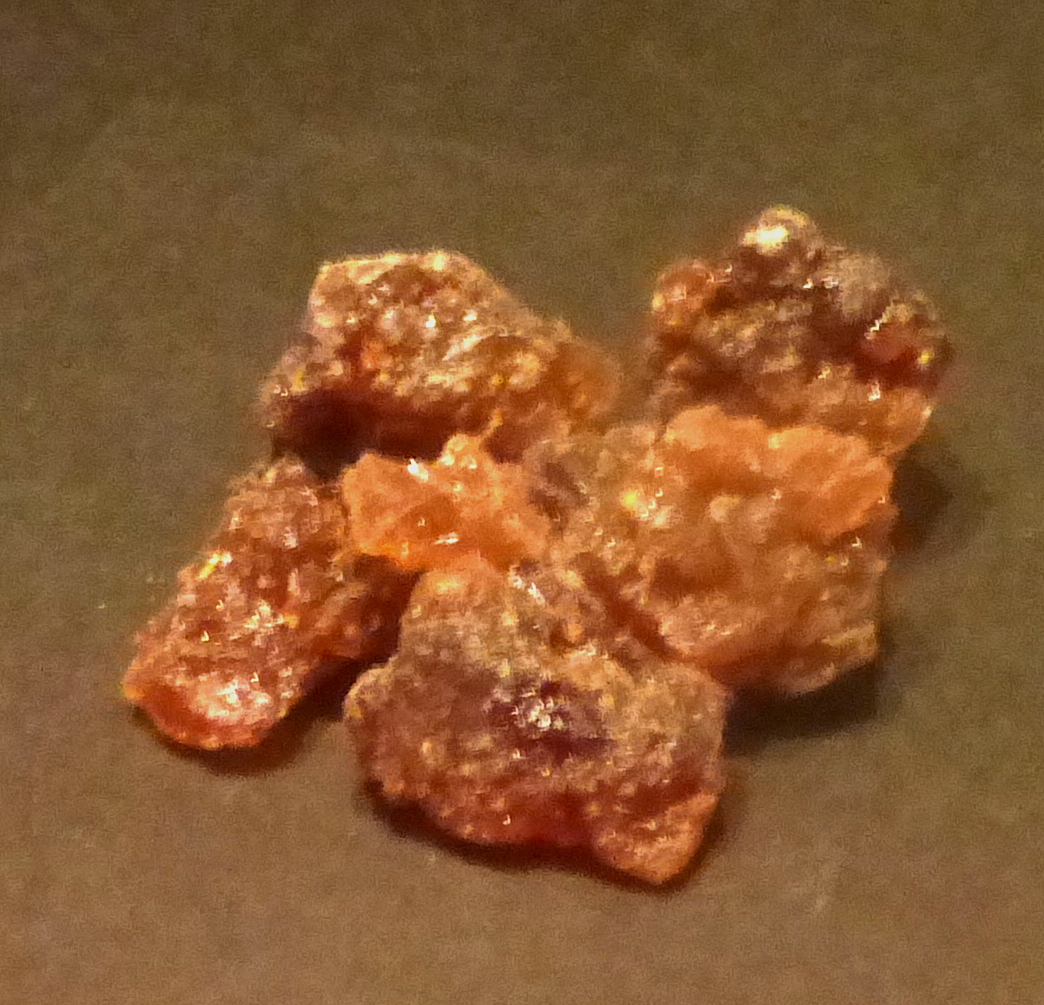 A cluster of rough reddish-orange lumps of dried myrrh resin on a dark surface